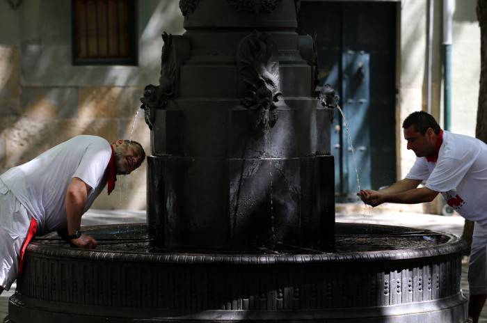Two men cool off with water from a fountain of Pamplona during a hot summer day at the San Fermin Festival on July 7, 2015. The festival is a symbol of Spanish culture that attracts thousands of tourists to watch the bull runs despite heavy condemnation from animal rights groups.   AFP PHOTO/ CESAR MANSO        (Photo credit should read CESAR MANSO/AFP/Getty Images)